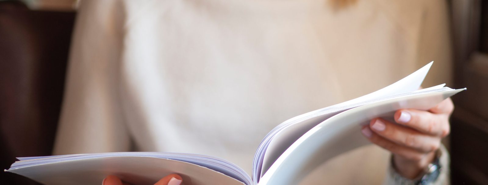 Woman reading a blank white magazine in caffe. Cropped body no face.